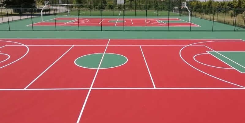 Basketball court in red and green acrylic with white playing lines and mesh fencing behind