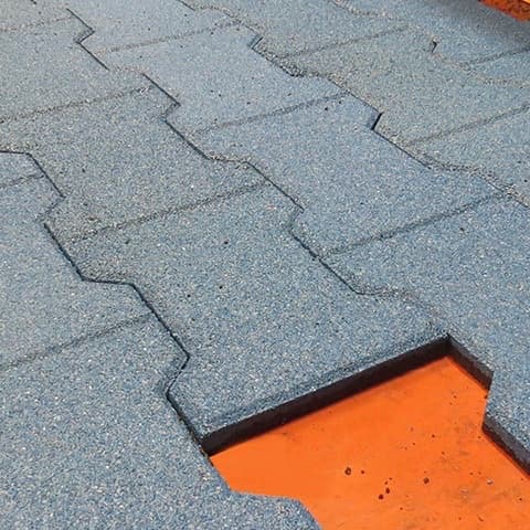 Interlocking rubber tiles being laid side by side over an orange base layer