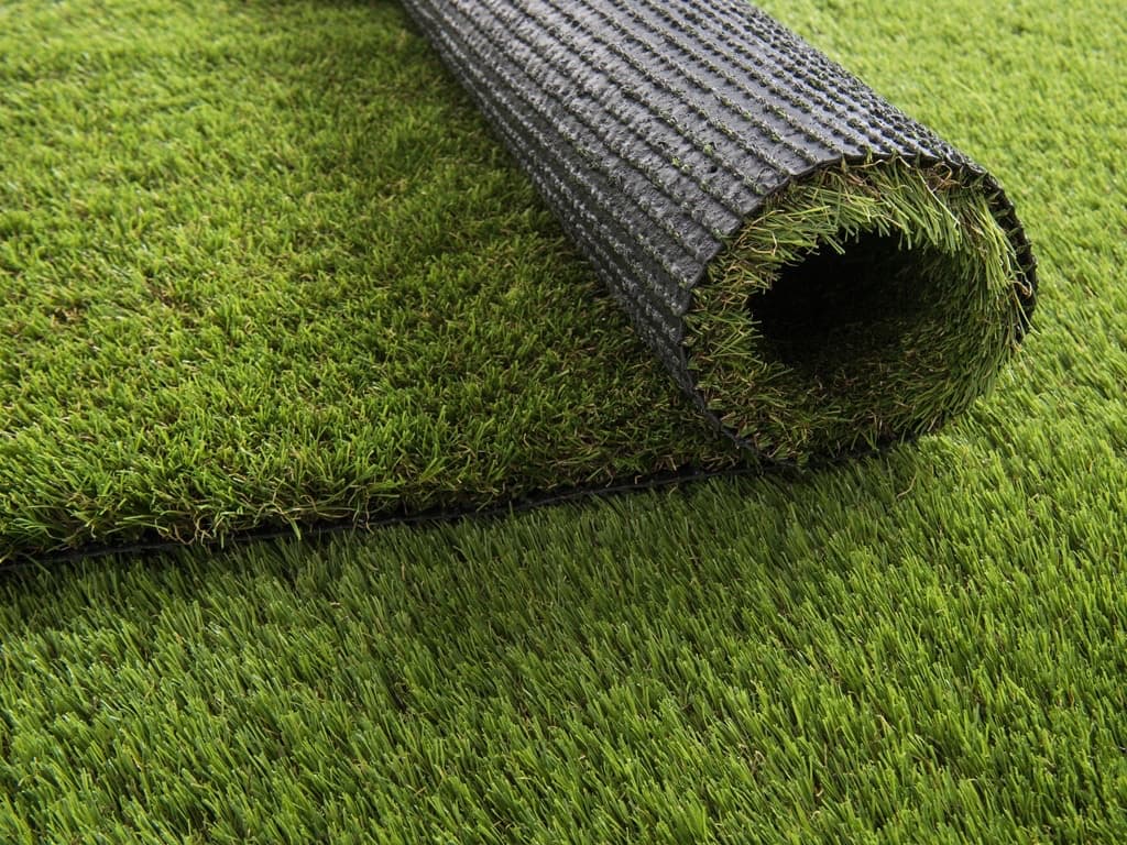 Artificial turf partly rolled back, showing the perforated backing beneath the pile