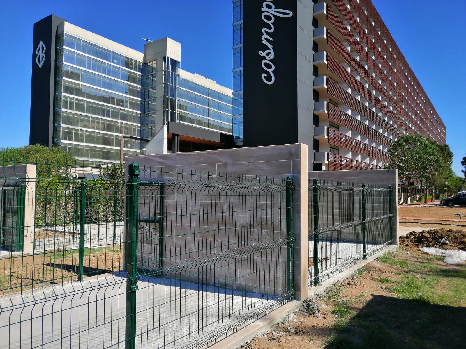Cosmopolitan otel binası önünde alçak duvar üzerine monte yeşil panel çit
