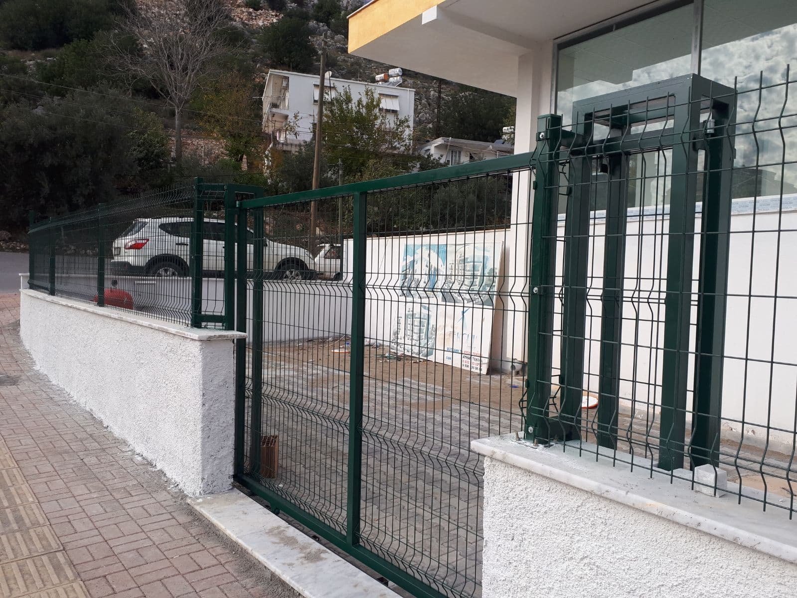 Alçak duvar üzerine monte edilmiş yeşil panel çit ve kanatlı bahçe kapısı